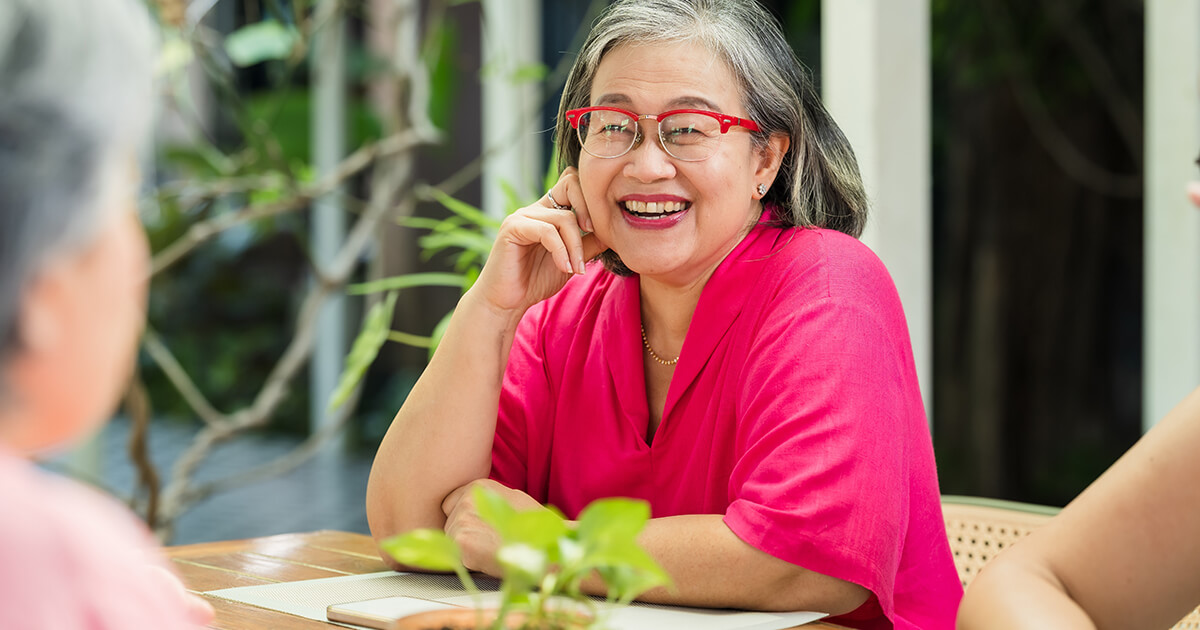 Elderly Asian woman smiles during restaurant reunion with close friend, sharing uplifting update, kind advice, emotional reassurance, warm companionship, relaxed brunch talk, later life connection.