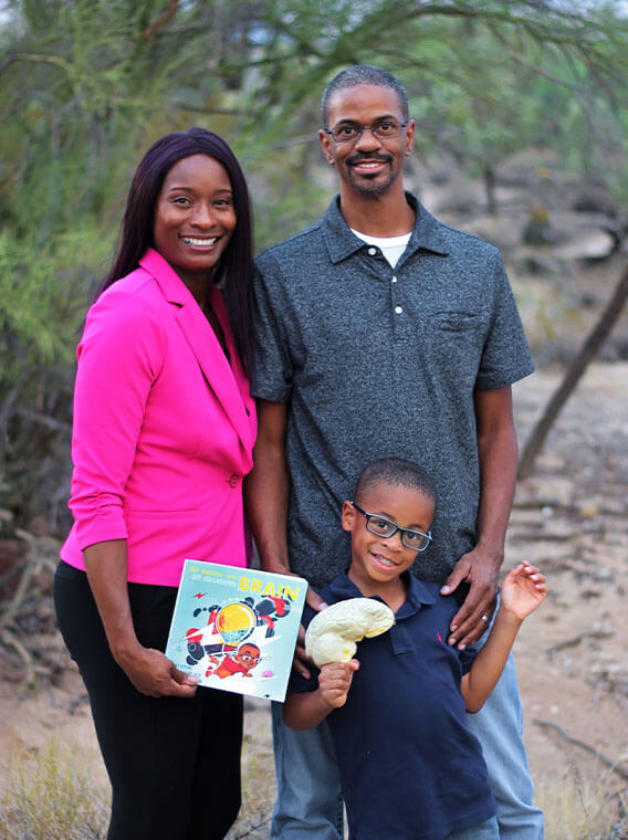Family standing outdoors with a child holding a brain model and a brain-themed children's book