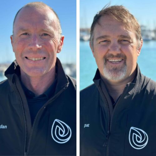 Side-by-side portraits of Brendan Cusick (left) and Pat Morrissey (right), both wearing black jackets with a white logo, smiling against a marina backdrop with blue water.