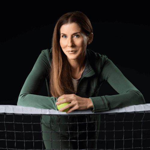 Tennis champion Monica Seles poses with a tennis ball, leaning on a net