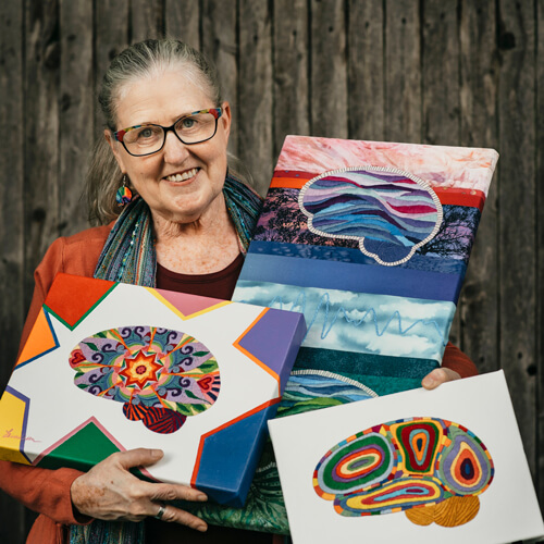 Photograph of mixed media artist, Laura Bundesen posing with her artwork depicting the human brain.