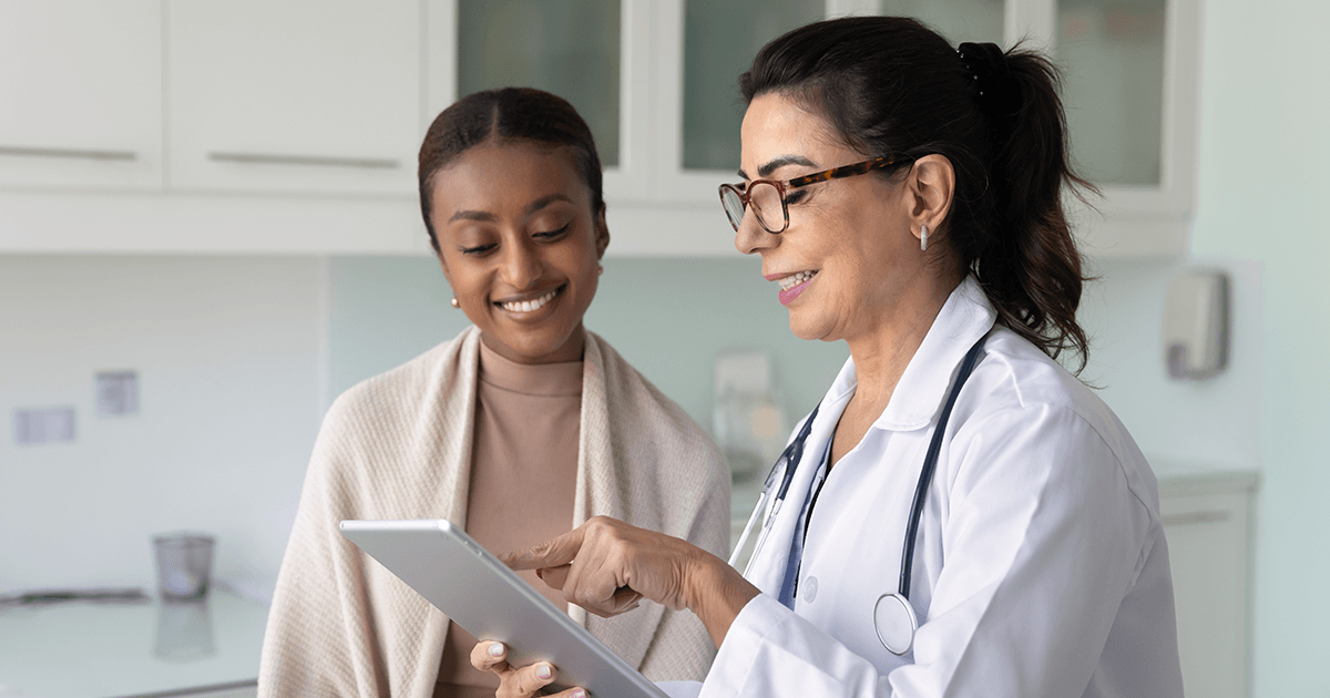 Happy doctor and young patient women watching medical examination electronic result on tablet, smiling, talking, reviewing and discussing content on digital device